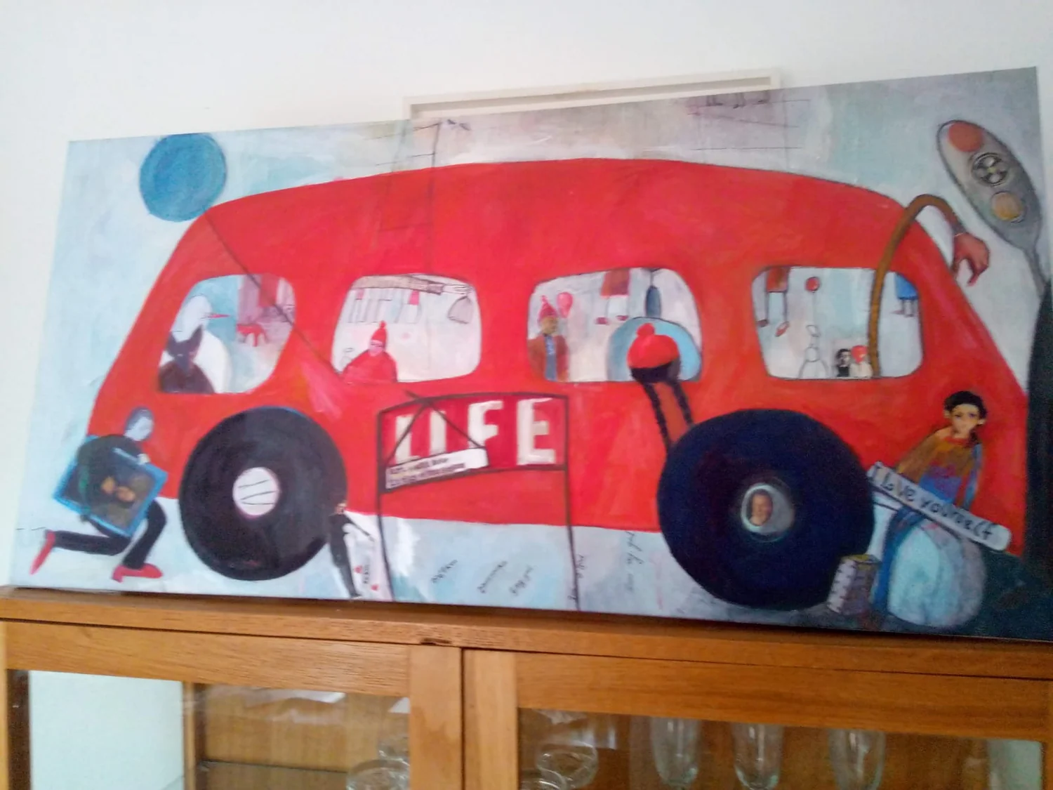 Large red bus painting with small figures inside and around the windows.